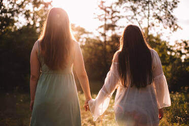 slow burn lesbian romance picture of two women holding hands walking through a park on a sunny day.