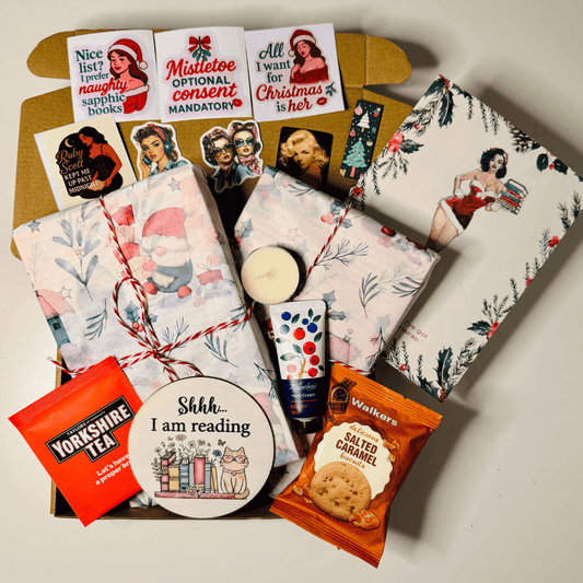 Festive lesbian gift box featuring lesbian romance book merchandise by lesbian romance fiction author Ruby Scott, including wrapped books, Christmas stickers with sapphic quotes, a candle, tea, biscuits, hand cream, and a “Shhh… I am reading” coaster — a cosy lesbian love story-themed Christmas bundle perfect for book lovers.