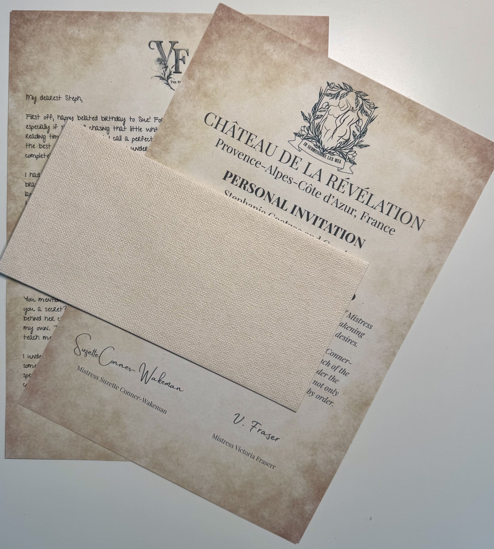 Two vintage-style documents partly covered by a textured beige envelope. One is a handwritten letter with the initials “VF” at the top, and the other is a formal invitation from “Château de la Révélation” in Provence, France. Signed by Mistress Suzette Conner-Wakeman and Mistress Victoria Fraser, the papers evoke an air of sensual mystery and exclusive romance.
