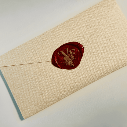 A textured beige envelope sealed with a glossy red wax stamp featuring the initials "VF" in gold, entwined with a botanical thistle motif. The elegant presentation evokes a sense of mystery and romance tied to the character Victoria Fraser.