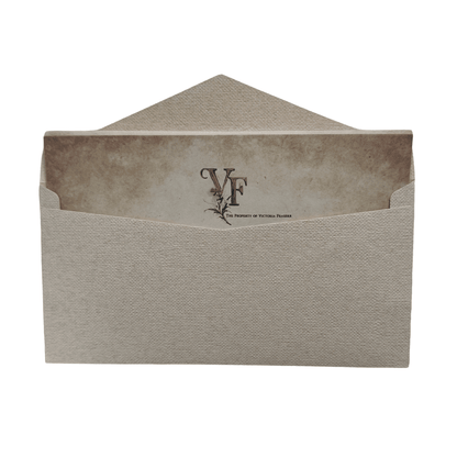A textured beige envelope holding a vintage-style letter marked with the initials "VF" and the phrase "The Property of Victoria Fraser." The letter has an aged paper look, evoking mystery, sensuality, and the refined world of lesbian romance fiction.