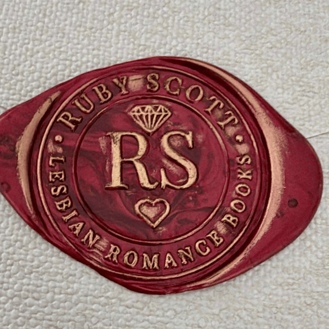 A red and gold wax seal featuring the initials "RS" in the centre, a diamond icon above, and a heart below. The outer ring reads "Ruby Scott • Lesbian Romance Books" in embossed text.