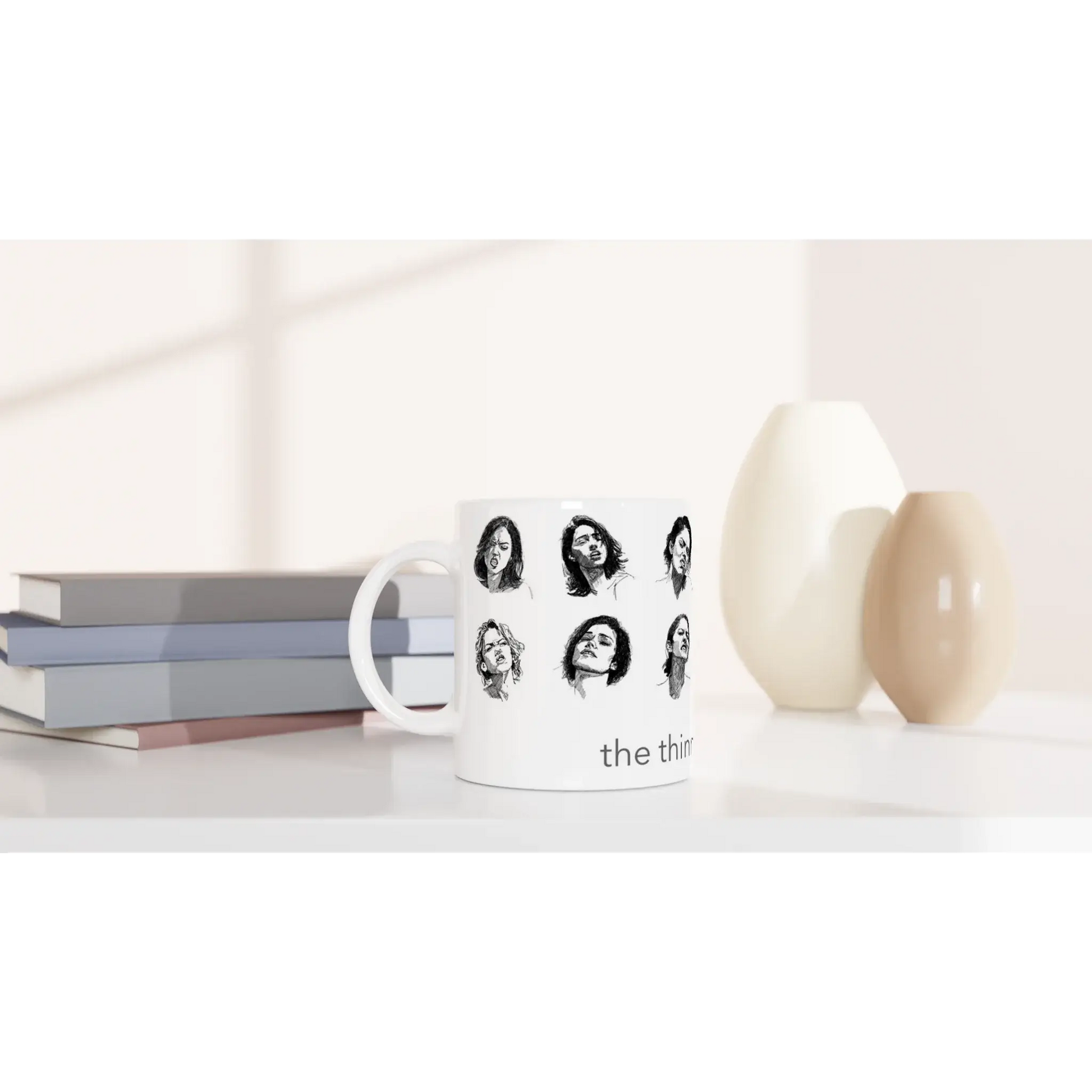 Smut reader mug with black and white illustrated faces placed beside stacked books on a minimalist shelf, styled lifestyle photo.